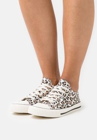 Baskets en toile à imprimé léopard avec semelles en caoutchouc blanches, lacets beiges et accents noirs, présentant un design à tige basse et une tige texturée.
