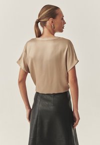 Beige satin topp med korta ärmar, parat med en svart läderkjol. Slät textur, minimal design och bakvy visas.