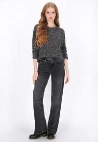 Zwarte textuurtrui, vergezeld van hoge zwarte jeans en zwarte enkellaarsjes. De outfit heeft een relaxte pasvorm en een casual ontwerp.