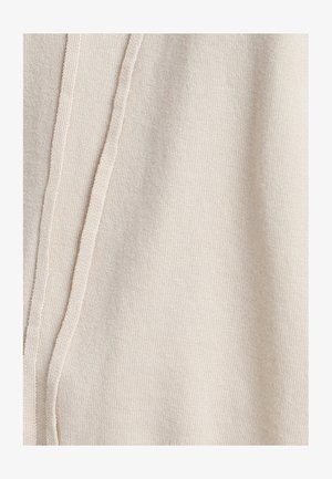 Beige Strickstoff mit einer weichen Textur, der an einer Seite eine vertikale Naht aufweist. Das Design ist einfach und minimalistisch.