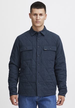 Dark blue quilted jacket with a button-up front, two chest pockets, and a collar. Made of soft fabric with a textured finish.