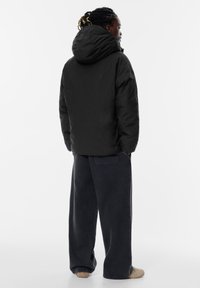 Giacca a vento nera, con cappuccio, design leggermente accorciato e tessuto testurizzato. Abbinata a jeans in denim scuro a gamba larga e scarpe beige.
