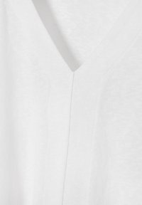 Tricou alb cu decolteu în V, realizat dintr-un material moale și texturat; prezintă o cusătură subtilă care se desfășoară pe mijloc și detalii minime de cusătură.