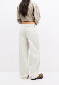 Jean beige crème à jambes larges en coton, doté d'une taille haute et de deux poches arrière. Associé à un haut court taupe.