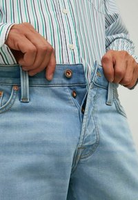 Heledad sinine denim teksad, millel on ees nööp sulgemine, vöölympärid ja kontrastsed õmblused. Kangas on veidi kulunud tekstuuriga.