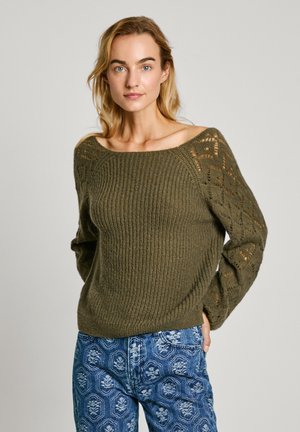 Maglione verde a maglia con scollatura ampia e maniche a motivo pizzo. Abbinato a jeans blu a fantasia. La texture è voluminoso e caldo.