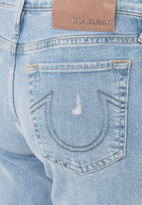 Jeans de denim azul claro con un distintivo patrón de costura en forma de U en el bolsillo trasero y una etiqueta de cuero que dice "True Religion."