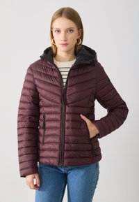Bordo puffer jakna s kapuljačom, s horizontalnim šavovima, zatvorenim prednjim džepovima i crnom podstavom. Nosi se preko prugaste majice.