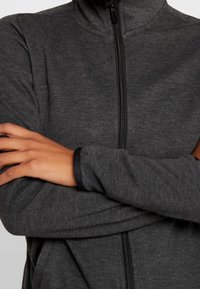 Veste zippée gris foncé avec un col montant, des manches longues agrémentées de poignets noirs et un tissu lisse et texturé.