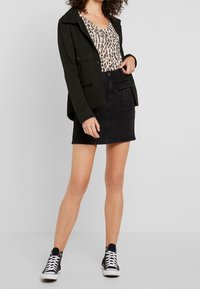 Falda de mezclilla negra con cintura alta, combinada con una blusa de estampado de leopardo y una chaqueta verde oscura; completada con zapatillas altas negras.