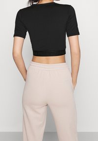 Černý krátký rukávový cropped top s těsným střihém a texturovaným páskem se znakem, kombinovaný se světle béžovými kalhotami s elastickým pasem.