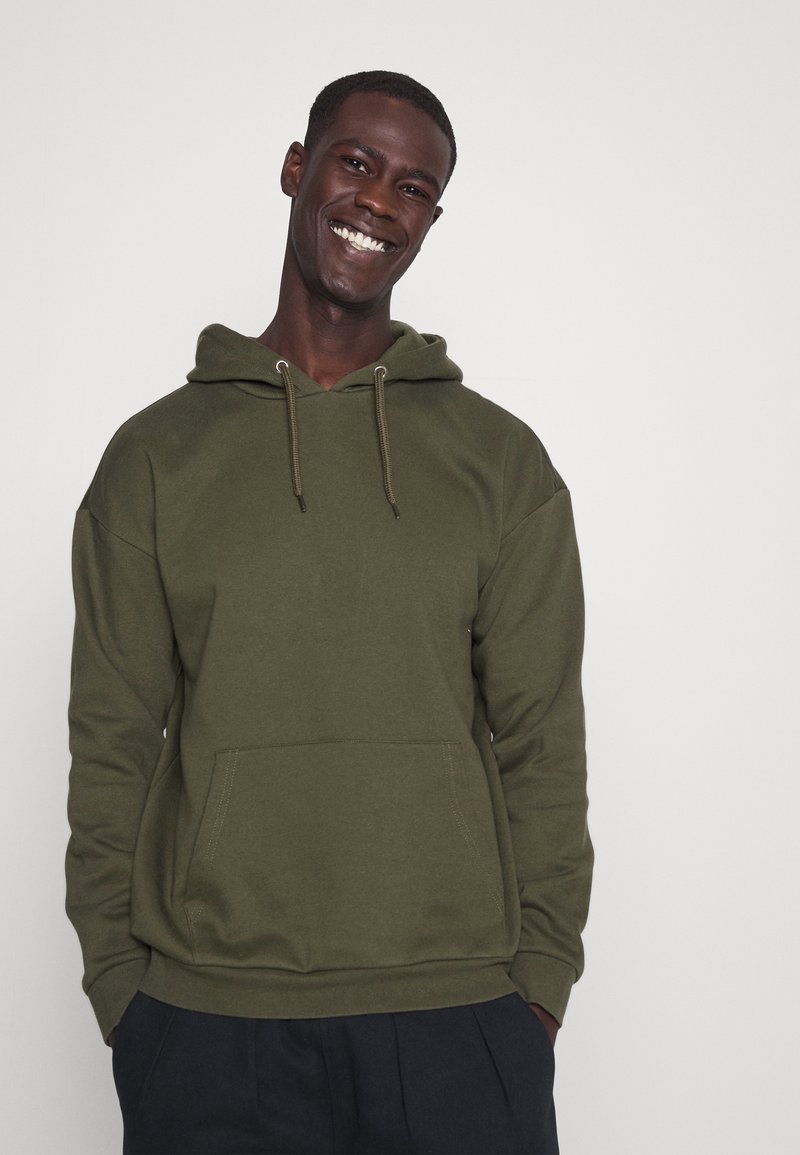 Oliwkowy hoodie wykonany z miękkiego materiału, z kieszenią z przodu, kapturem ze sznurkiem i ściągaczami przy mankietach oraz hemie.