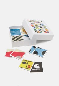 Kortspil med en hvid æske, der har farverige grafiske mønstre på toppen. Indeni viser firkantede kort forskellige motiver i stærke farver og teksturer.