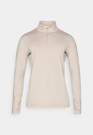 Beige long-sleeve top with a half-zip collar, made from smooth, lightweight fabric. Features a subtle logo on the chest.