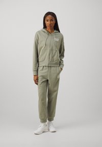 Svijetlozelena zip-up hoodie i odgovarajući trenirci, izrađeni od mekog materijala, s prednjim džepom, rebrastim manžetama i logotipom na prsima i nogavici.