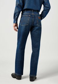 Jeans in denim blu scuro con una vestibilità a gamba dritta, dotati di tasche posteriori con un design di cucitura distintivo e un'etichetta in pelle sulla vita.