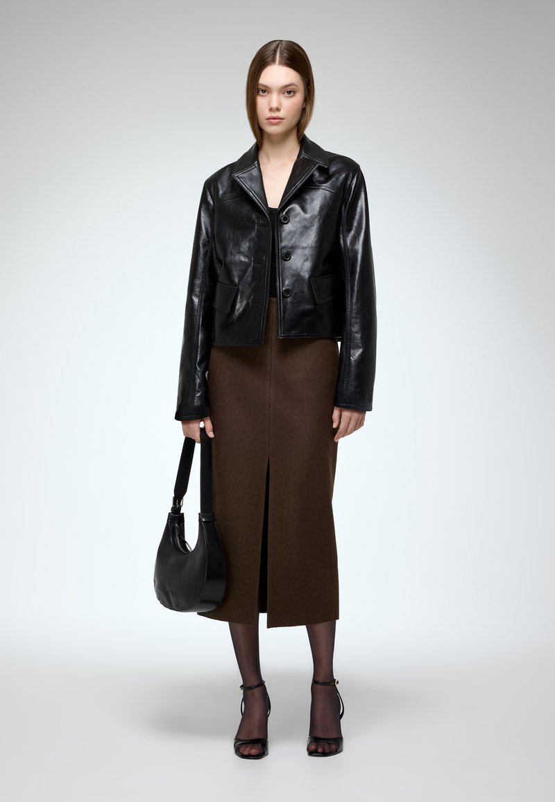 Black leather cropped jacket, brown fitted skirt with a front slit, black handbag, and black heeled sandals with ankle straps.