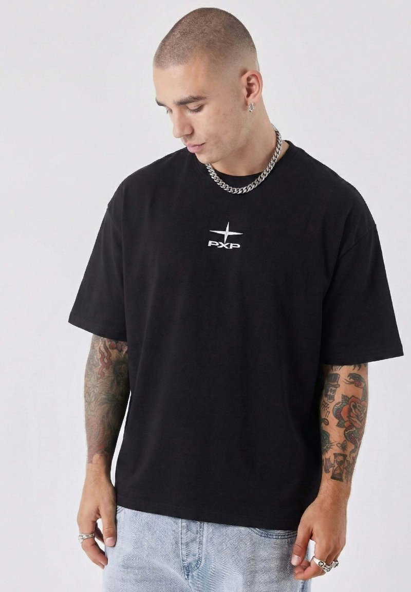 Black short-sleeve t-shirt featuring a white "PXP" logo on the chest, made of cotton with a relaxed fit. Worn with light blue denim jeans.