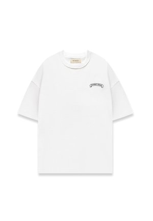 Camiseta blanca texturizada de manga corta con cuello redondo y un pequeño logo negro "RETERNITY ATELIER" en el lado izquierdo del pecho.
