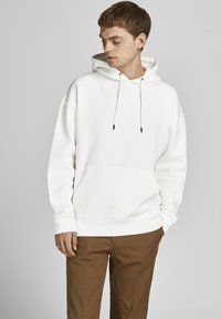 Witte hoodie met een voorzak, koordjes en geribbelde manchetten, gecombineerd met een paarse broek. Heeft een relaxte pasvorm en een zachte textuur.