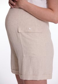 Beige linnen shorts met een zijzak met knoopsluiting, omgeslagen zoom en een relaxte pasvorm. De stof heeft een gestructureerde uitstraling.