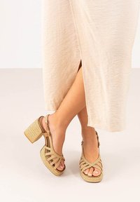 Sandalias de cuña beige con textura tejida, diseño de punta abierta y múltiples correas. El tacón grueso proporciona estabilidad y cuenta con una correa para el tobillo ajustable.