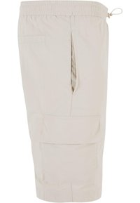 Lys beige cargo-shorts med elastisk linning og snor, med sidelommer og en lommepatch på benet. Glatt stofftekstur.