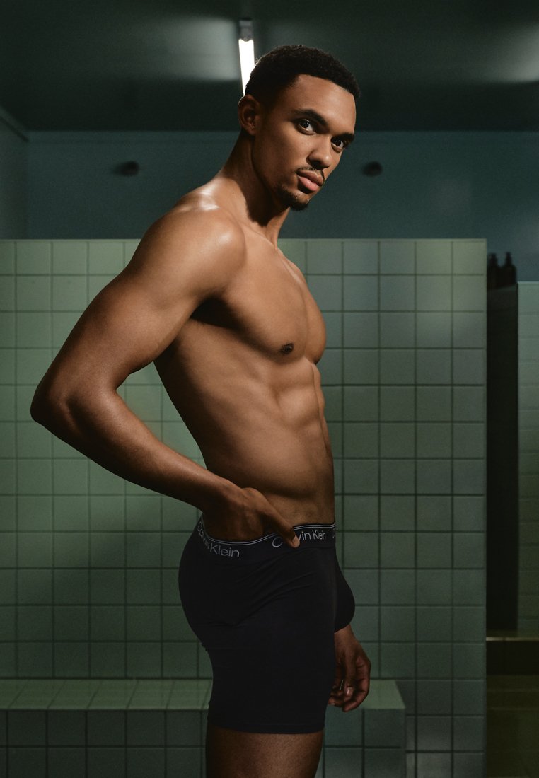 Zwarte boxershorts van Calvin Klein met een logo-elastieken band, gedragen door een model dat een aansluitend ontwerp, een gladde textuur en een atletisch postuur laat zien, in een betegelde omgeving.