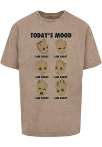 Pruun puuvillane T-särk, millel on kuus Grooti tegelaskuju illustreerimist erinevate näoilmetega, tekstide "TÄNA'S MEELDETULEK" ja "MA OLEN GROOT" kohal.