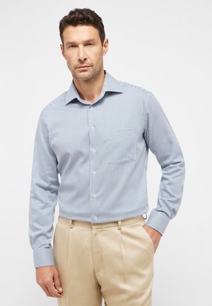 Gestreiftes blau-weißes Hemd mit Knopfverschluss, kragen, langen Ärmeln und einer Brusttasche, kombiniert mit beigefarbenen Hosen.