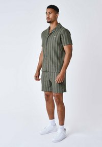 Camicia a maniche corte a righe verdi e pantaloni corti abbinati, realizzati in un tessuto testurizzato, abbinati a scarpe da ginnastica bianche e calzini alla caviglia.