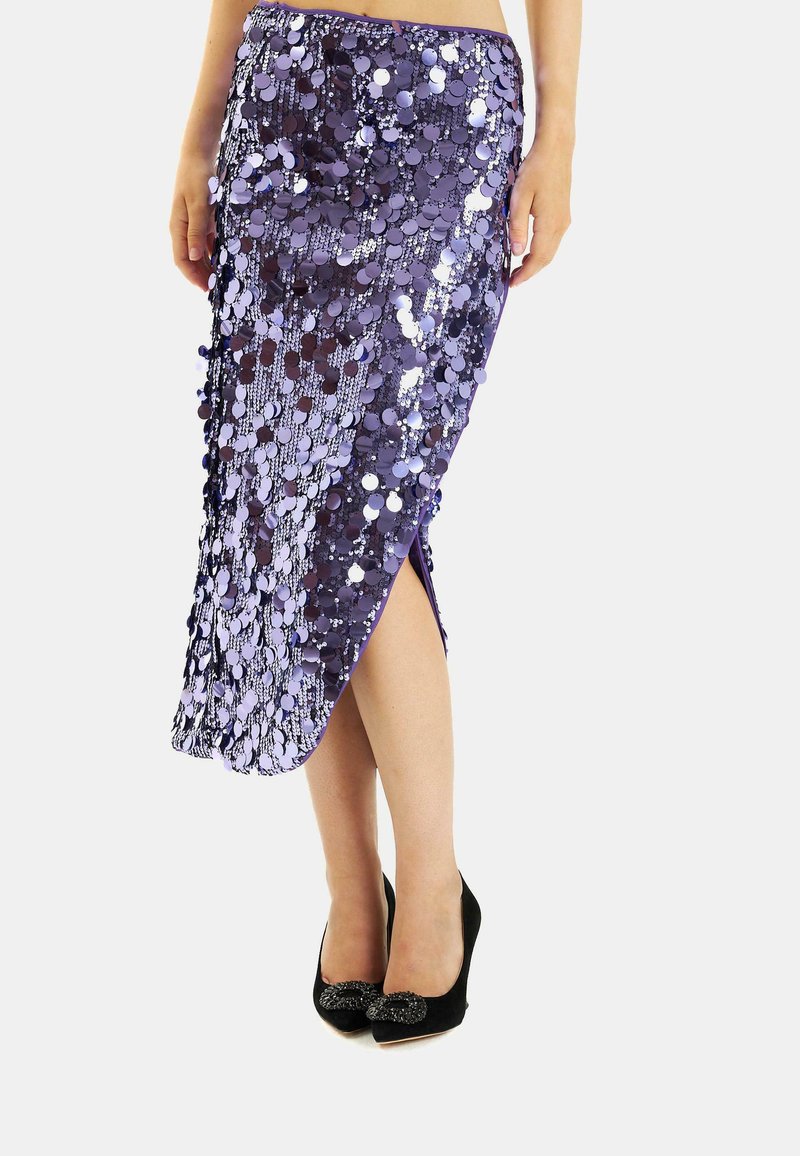 Fioletowa spódnica z cekinami, z wysokim rozcięciem, cechująca się błyszczącym wykończeniem i lekką teksturą, połączona z czarnymi szpilkami.