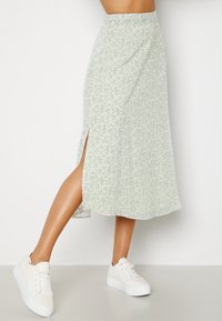 Falda midi verde claro con estampado floral y una abertura lateral, hecha de una tela ligera y fluida. Combinada con zapatillas blancas.