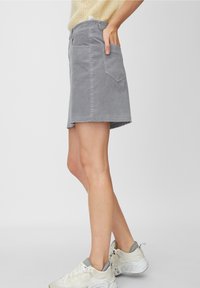 Minifalda de mezclilla gris con dobladillo deshilachado, bolsillos a ambos lados y silueta ajustada. Llevada con zapatillas blancas.