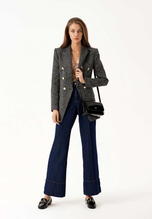 Blazer grigio doppiopetto con bottoni dorati, abbinato a pantaloni in denim scuri a gamba larga e borsa a tracolla in pelle nera. Tessuto liscio e strutturato.