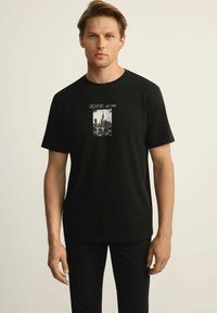 Czarna bawełniana koszulka z grafiką przedstawiającą panoramę miasta z napisem "OCHNIK EST. 1999" powyżej. Krótkie rękawy, okrągły dekolt.