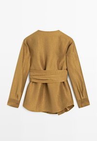 Camicia a maniche lunghe in marrone dorato, con vita con cintura. Tessuto liscio con collo semplice e polsini abbottonati. Vestibilità sartoriale.