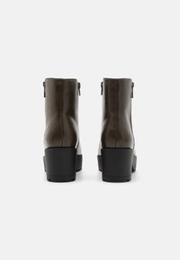 Stivaletti in pelle marrone con finitura testurizzata, tacco a piattaforma nero rialzato, doppie cerniere e un design elegante e minimalista.