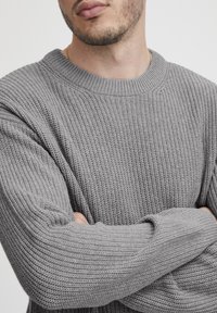 Harmaa neulepusero, jossa on tekstuuri kuvio, pyöreä kaula-aukko ja pitkät hihat, varustettuna resorihihansuilla ja hienovaraisilla saumoilla.