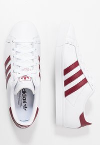 Vita sneakers med tre vinröda ränder. Har vadderad tunga, runda skosnören och gummisula. Överdel i texturerat läder med logotyp.