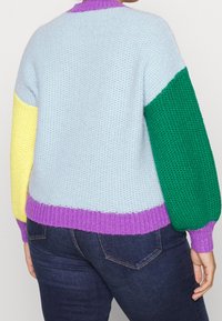 Pull coloré avec un corps bleu clair, des manches vertes, jaunes et violettes, un tricot texturé et des poignets côtelés.