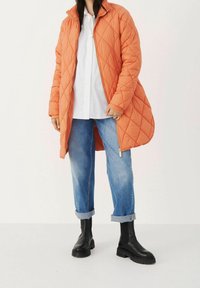 Quiltet orange jakke med høj krave og lynlås, parret med opsmallede lyseblå jeans og sorte ankelstøvler. Ren, struktureret design.