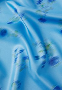 Lichtblauwe stof met een gladde textuur, met vervaagde bloemenpatronen in blauwe en groene tinten. Zacht, lichtgewicht materiaal met een lichte glans.