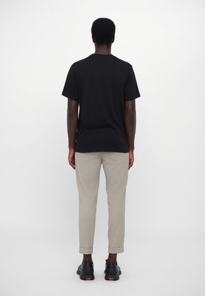 Black short-sleeve t-shirt paired with light beige tailored trousers, featuring rolled cuffs and black footwear with a colored accent.