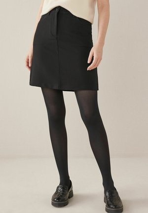 Zwarte A-lijn rok met knoopsluiting aan de voorkant, gemaakt van gladde stof. Draagt zwarte, ondoorzichtige panty's en stevige zwarte schoenen.