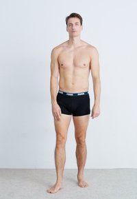 Schwarze Baumwoll-Boxershorts mit einem kontrastierenden Bund, der das Puma-Logo trägt, getragen von einem männlichen Model, das aufrecht vor einem neutralen Hintergrund steht.