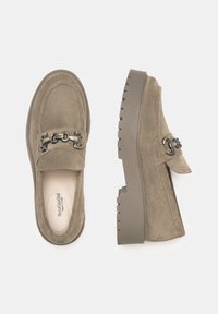 Mocassins en daim marron avec une semelle épaisse, ornés d'une chaîne décorative sur le dessus. Intérieur lisse et détails de couture sur les côtés.