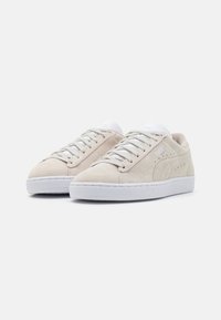 Baskets en daim beige clair avec lacets blancs et semelle blanche. Bout arrondi, design minimaliste, avec un petit logo et des accents perforés.