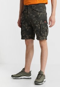 Pantaloni cargo camouflage in verde scuro e nero con molte tasche, tessuto resistente e una vestibilità comoda. Indossati con sneakers verde oliva.