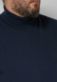 Marineblauer Rollkragenpullover mit geripptem Kragen und weicher Textur, mit einer Nahaufnahme des Kragens und des Oberkörpers.